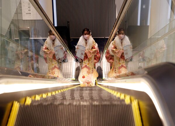 امرأة ترتدي كيمونو وقناعًا واقٍ يركب سلمًا متحركًا في مكان الاحتفال بعيد بلوغ سن الرشد، وسط تفشي فيروس كورونا في طوكيو، اليابان، 10 يناير 2022. - سبوتنيك عربي