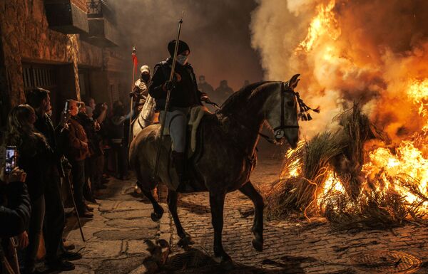 امرأة تركب حصانًا بجوار نار خلال مهرجان لاس لومينارياس التقليدي في قرية سان بارتولومي، إسبانيا 16 يناير 2022 - سبوتنيك عربي
