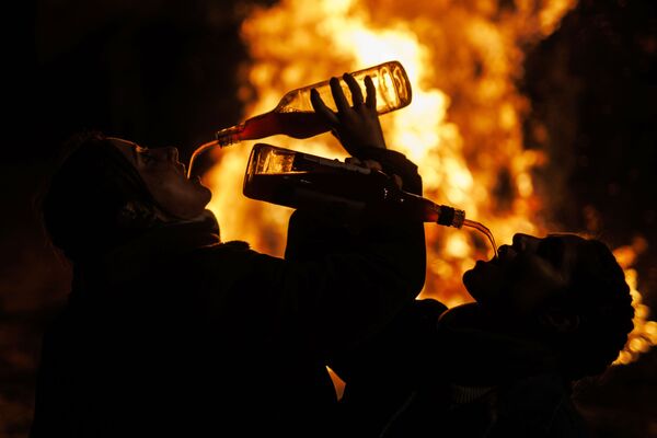 أشخاص يشربون النبيذ على خلفية نيران مشتعلة أثناء احتفال لاس لومينارياس السنوي عشية يوم القديس أنتوني، القديس الراعي للحيوانات في إسبانيا  في قرية سان بارتولومي دي بيناريس، شمال غرب مدريد، 16 يناير 2022. - سبوتنيك عربي
