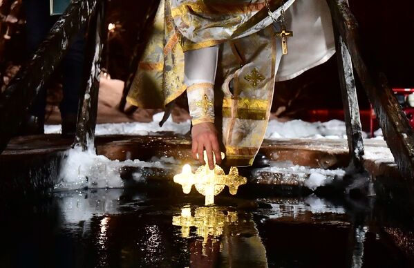رجل دين يُدخل صليبًا في بركة مياه جليدية في منطقة ترويتسكي الإدارية في موسكو بمناسبة عيد الغطاس، روسيا 18 يناير 2022 - سبوتنيك عربي