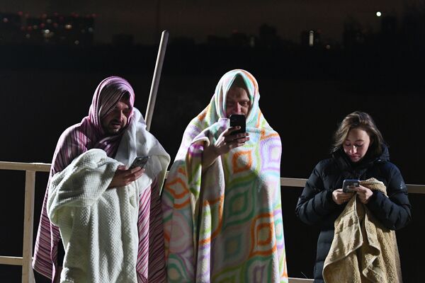 غطى المشاركون في عيد الغطاس يغطون أنفسهم بالمناشف والغطاء الدافئ بعد الغطس في حديقة ستروغينو في موسكو، ويلتقطون الصور للذكرى، روسيا 18 يناير  2022 - سبوتنيك عربي