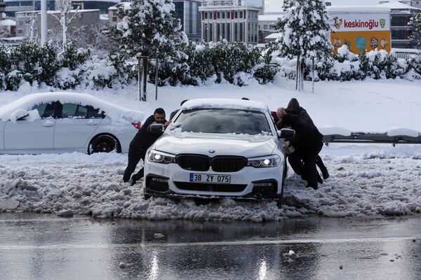 أشخاص يدفعون سيارة عالقة في شارع مغطى بالثلوج في إسطنبول، 25 يناير 2022. سارعت فرق الإنقاذ في إسطنبول لتنظيف الطرق التي توقفت بعد أن ضربت موجة برد شديدة وعواصف ثلجية معظم أنحاء تركيا. - سبوتنيك عربي