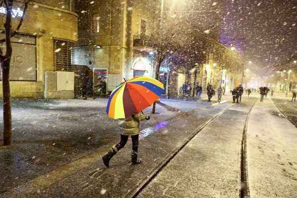 شخص يسير مع مظلة مع بدء تساقط الثلوج لأول مرة خلال عاصفة ثلجية في القدس، 26 يناير 2022. - سبوتنيك عربي