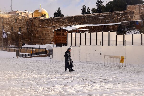 رجل يهودي أرثوذوكسي يسير على الثلج بالقرب من الحائط الغربي في صباح ثلجي في البلدة القديمة في القدس، 27 يناير  2022. - سبوتنيك عربي