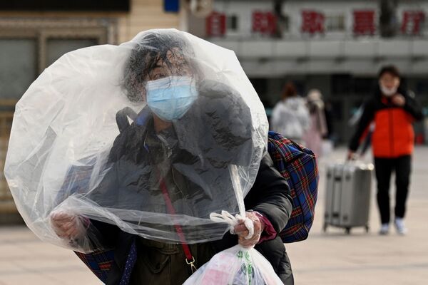 امرأة تستخدم كيسًا بلاستيكيًا كغطاء تمشي خارج محطة سكة حديد في بكين، 26 يناير 2022 ، قبل أكبر عطلة في العام، السنة القمرية الجديدة، والتي تبشر بعام النمر. - سبوتنيك عربي