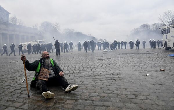 رجل يجلس على الرصيف بينما تواجه الشرطة المتظاهرين خلال مظاهرة ضد إجراءات كورونا في بروكسل، بلجيكا 23 يناير 2022. - سبوتنيك عربي