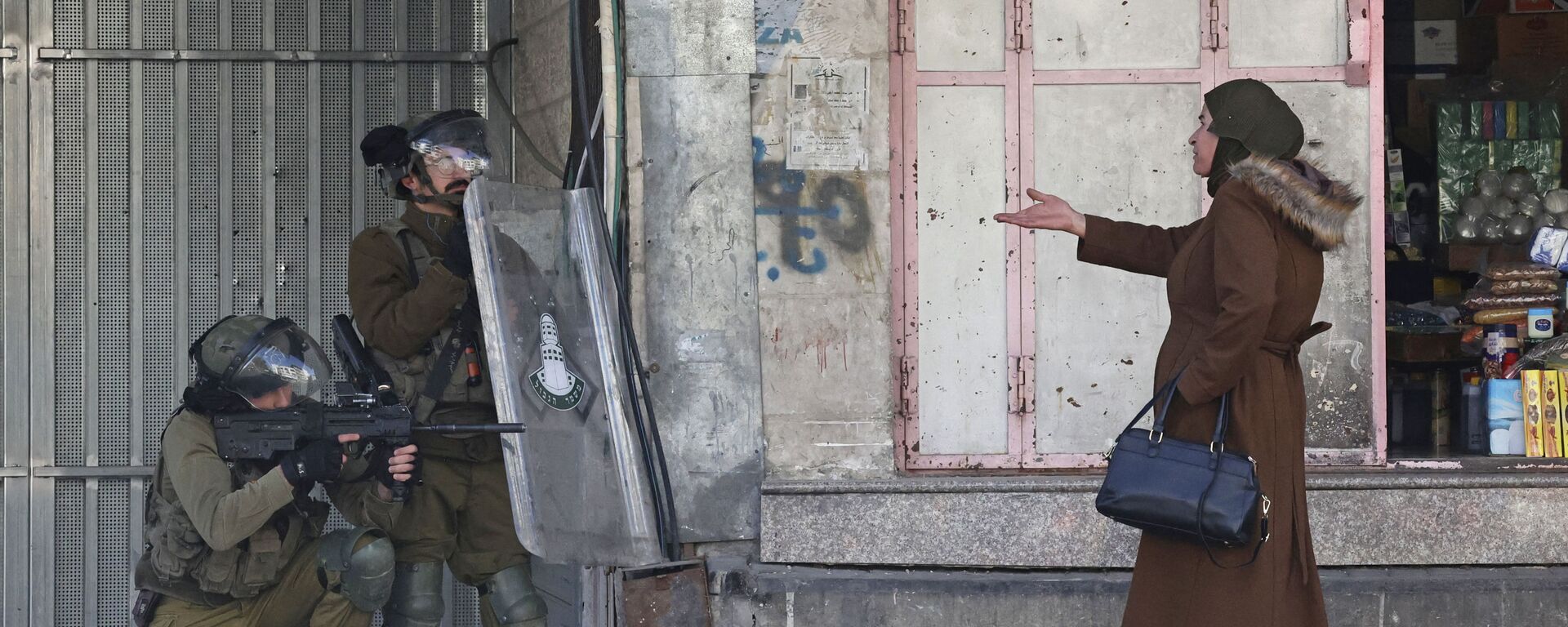 امرأة تشير إلى قوات الأمن الإسرائيلية التي أطلقت الرصاص المطاطي لتفريق فلسطينيين يلقون الحجارة وسط اشتباكات في بلدة الخليل بالضفة الغربية المحتلة، 9 فبراير 2022.  - سبوتنيك عربي, 1920, 22.09.2022