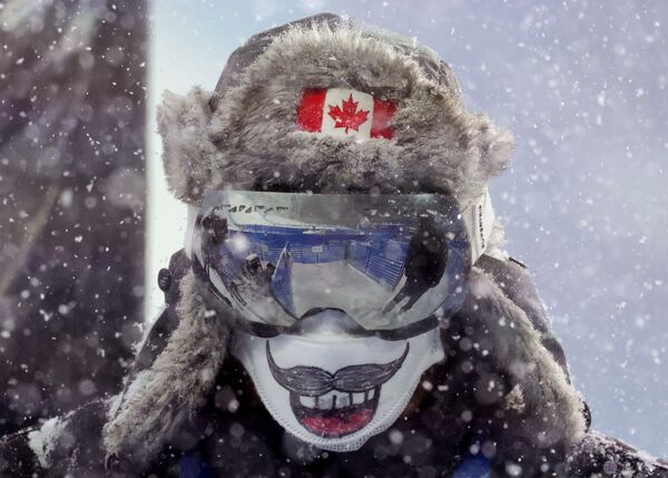 أحد أفراد طاقم هيئة الإذاعة الكندية يرتدي قناعًا أثناء تساقط الثلوج بكثافة. خلال مسابقات التزلج الحر، فئة التزلج الهوائي للسيدات في حديقة جنتناغ الجليدية، تشانغجياكو، الصين، أولمبياد بكين 2022، 13 فبراير 2022.  - سبوتنيك عربي