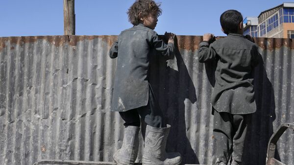 أولاد أفغان ينظرون فوق حاجز حديدي عند الأشخاص الذين يتلقون الإمدادات الغذائية أثناء توزيع المساعدات الإنسانية للعائلات المحتاجة في كابول، أفغانستان، 16 فبراير 2022. - سبوتنيك عربي