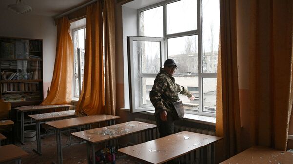 أحد عناصر الشرطة التباع لجمهورية دونيتسك الشعبية في الفصل الدراسي في مدرسة غورلوفكا، الذي تضرر من جراء القصف الأوكراني، 25 فبراير 2022 - سبوتنيك عربي