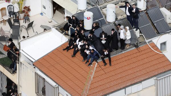 مشيعون يهود متشددون ينتظرون على سطح أحد المنازل خارج مقبرة بونيفيج في مدينة بني باراك بالقرب من تل أبيب، وسط إسرائيل، خلال جنازة الحاخام الحريديم حاييم كانيفسكي، 20 مارس 2022 - سبوتنيك عربي