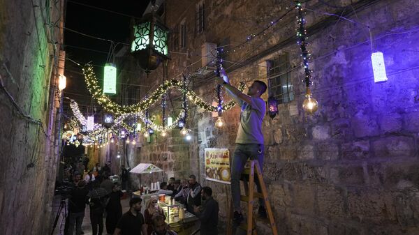 رجل فلسطيني يعلق أضواء زخرفية استعدادًا لشهر رمضان المبارك، في شوارع البلدة القديمة في القدس، 1 أبريل 2022. - سبوتنيك عربي