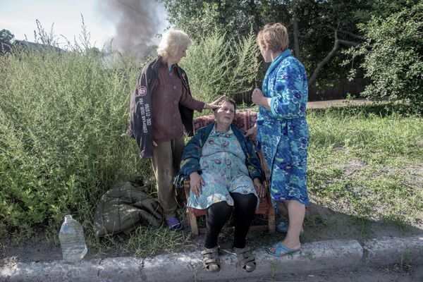 عواقب قصف الجيش الأوكراني لسلافيانسك. الجيران يساعدون امرأة اشتعلت النيران في منزلها بعد إصابتها بقذيفة. - سبوتنيك عربي