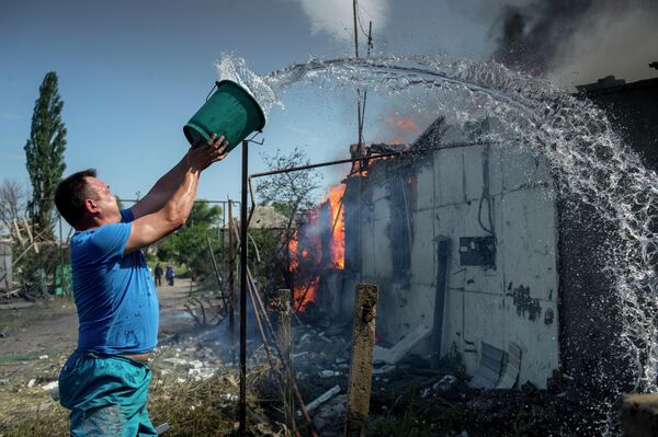  يوليو/ تموز 2014. مواطن في قرية لوغانسكايا يطفئ النار في بيته بعد قصف من قبل الطيران الأوكراني. - سبوتنيك عربي