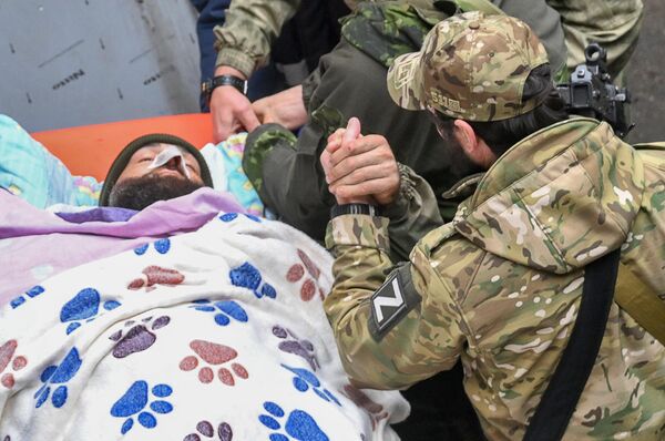 جندي روسي يدعم زميله الجريح ، الذي يُنقل على نقالة إلى سيارة إسعاف من مستشفى منطقة نوفوازوفسك المركزية لإجلائه لاحقًا إلى روسيا. - سبوتنيك عربي