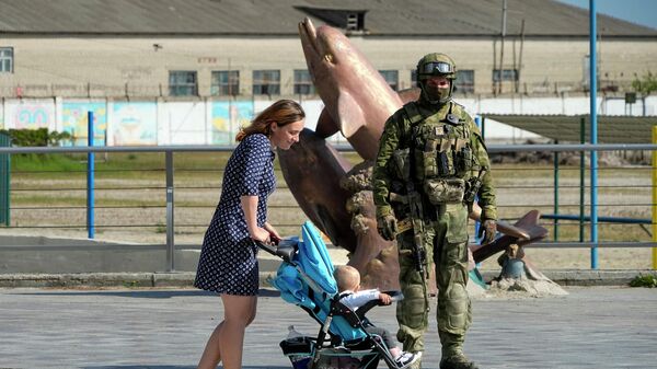 امرأة مع طفلها تسير من أمام جندي روسي عند جسر على البحر الأسود في خيرسون، منطقة خيرسون، جنوب أوكرانيا، 20 مايو 2022 - سبوتنيك عربي