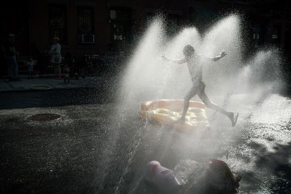 طفل يبرد نفسه في رذاذ الماء من صنبور إطفاء الحرائق خلال حفلة في حي بروكلين بنيويورك، 21 مايو 2022 - سبوتنيك عربي