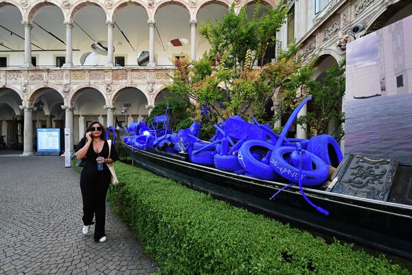 زائرة تمر بجوار معروضة فنية قم بتنظيف المياة: من فضلك (Clean Water: Please)، من تصميم (Marco Nereo Rotelli مع Ever in Art)، وهي عبارة عن غندول (قارب طويل ورقيق في إيطاليا) غمرته النفايات المستخرجة من أعماق مياه البندقية وتم تلوينها بالأزرق، في إطار معرض ديزاين فير (Design Fair) في ميلانو، إيطاليا، 6 يونيو 2022. - سبوتنيك عربي