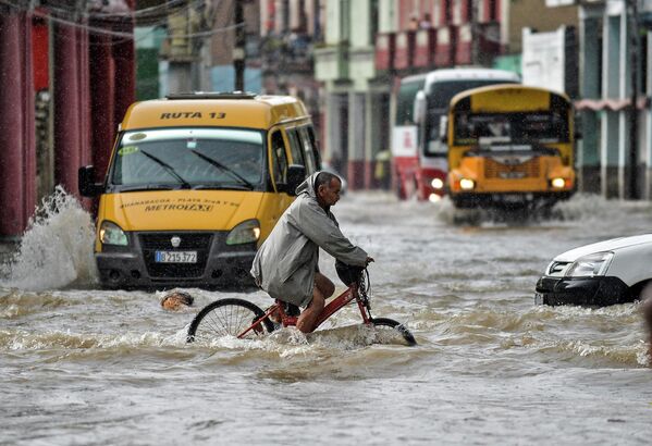 رجل يركب دراجته على طول شارع غمرته المياه في هافانا، بعد هطول أمطار غزيرة، العاصمة الكوبية هافانا، في 8 يونيو 2022. - سبوتنيك عربي