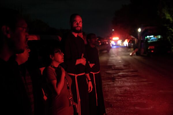 كهنة محليون من أبرشية سان أنطونيو يقفون بالقرب من مكان الحادث حيث تم اكتشاف جرار ومقطورة مع مهاجرين بالداخل خارج سان أنطونيو، تكساس في 27 يونيو 2022. - سبوتنيك عربي
