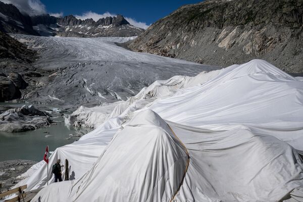يقف متجول بجانب الرغوة العازلة التي تغطي جزءًا من نهر الرون الجليدي لمنعه من الذوبان بجوار البحيرة الجليدية، التي تشكلت بسبب ذوبان النهر الجليدي إثر الاحتباس الحراري، بالقرب من غليتش، في جبال الألب السويسرية، في 8 يوليو 2022 - سبوتنيك عربي