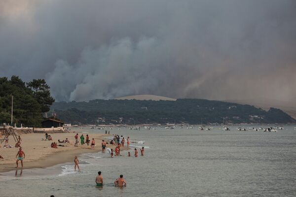تُظهر هذه الصورة التي التقطت في 18 يوليو 2022 الناس يسبحون على شاطئ مولو بينما يتصاعد الدخان من حريق الغابة في لا تيست دو بوخ، التي شوهدت من أركاشون، أمام الكثبان الرملية بيلات. - سبوتنيك عربي