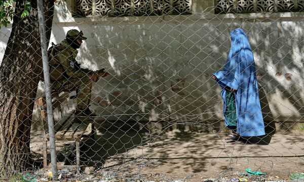 مقاتل من &quot;طالبان&quot; يقف حارسا بينما تدخل امرأة مكتب الجوازات الحكومي، في كابو ، أفغانستان، 27 أبريل 2022. أمرت قيادة &quot;طالبان&quot; الأفغانية جميع النساء الأفغانيات بارتداء البرقع في الأماكن العامة. المرسوم بتاريخ 7 مايو شمل قيودًا مماثلة على النساء خلال حكم &quot;طالبان&quot; السابق المتشدد بين عامي 1996 و2001. - سبوتنيك عربي