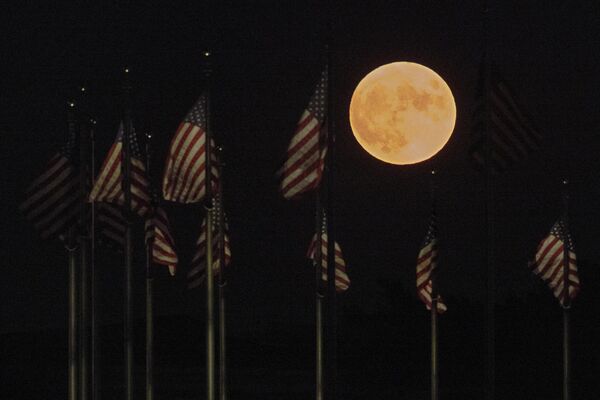 يرتفع القمر خلف أعلام الولايات المتحدة عند قاعدة نصب واشنطن التذكاري في 11 أغسطس 2022 في واشنطن العاصمة. ما يسمى بقمر الحفش هو القمر العملاق الرابع والأخير لعام 2022 - سبوتنيك عربي