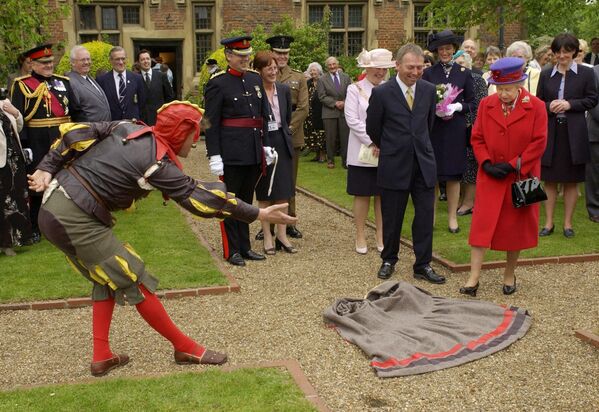 تمت دعوة ملكة بريطانيا إليزابيث الثانية (على اليمين) للوقوف على عباءة ألقيت عند قدميها من قبل الأحمق الإليزابيثي، الملقب بييت كوبر، في إيستبوري مانور هاوس أثناء زيارتها لليوبيل الذهبي إلى شرق لندن في 9 مايو 2002. - سبوتنيك عربي