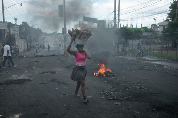 بائع متجول يمر عبر حاجز أقامه المتظاهرون للاحتجاج على ارتفاع أسعار الوقود ولمطالبة رئيس الوزراء الهايتي أرييل هنري بالتنحي، في بورت أو برنس، هايتي، 19 سبتمبر  2022. - سبوتنيك عربي
