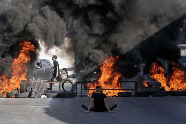 فلسطينيون يشعلون إطارات السيارات في الموقع حيث أطلق الجيش الإسرائيلي النار على فلسطينيين وقتلهما في مخيم الجلزون للاجئين بالقرب من مدينة رام الله ، الضفة الغربية، يوم 3 أكتوبر  2022 - سبوتنيك عربي