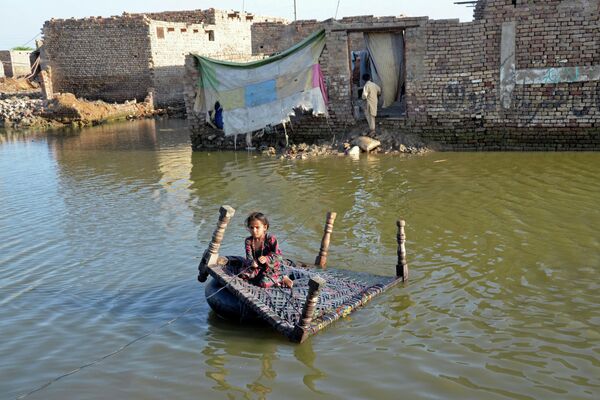 فتاة تجلس على سرير أطفال وهي تعبر الشارع الذي غمرته مياه الفيضانات في صحبت پور في منطقة جعفر آباد في مقاطعة بلوشستان، باكستان في 4 أكتوبر 2022. - سبوتنيك عربي