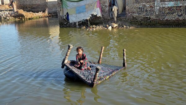 فتاة تجلس على سرير أطفال وهي تعبر الشارع الذي غمرته المياه في صحبت پور في منطقة جعفر آباد في مقاطعة بلوشستان، باكستان في 4 أكتوبر 2022. - سبوتنيك عربي