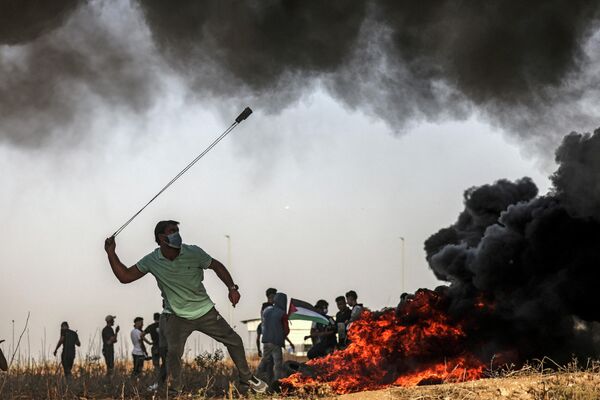متظاهر فلسطيني يستخدم المقلاع لرشق الحجارة عبر الحدود مع إسرائيل شرقي مدينة غزة، خلال اشتباكات مع القوات الإسرائيلية في أعقاب مظاهرة على طول الحدود، في 25 أكتوبر 2022 - سبوتنيك عربي