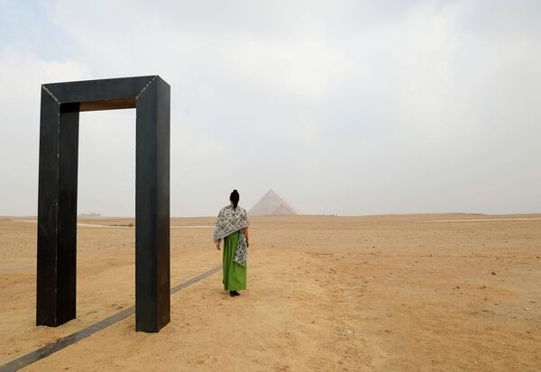 امرأة تسير أمام عمل فني إيطالي إيميليو فيرو، أطلق عليه اسم بوابة النور على هضبة الأهرامات في الجيزة في 27 أكتوبر 2022  - سبوتنيك عربي