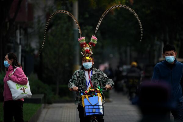رجل يرتدي كمامة طبية وغطاء رأس زي الملك القرد يركب مقيمين ملثمين في أحد شوارع بكين، الصين 2 نوفمبر 2022 - سبوتنيك عربي