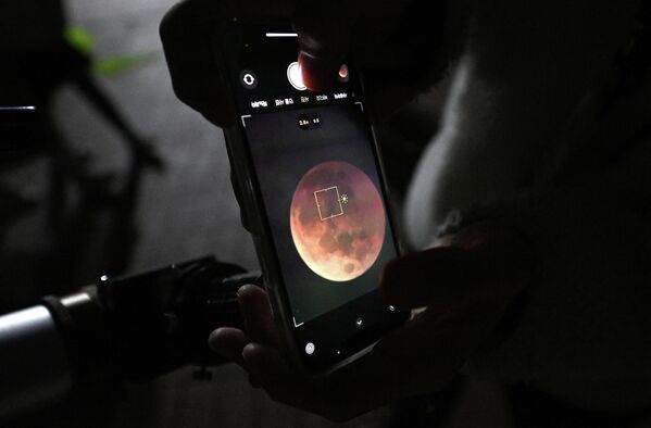 رجل يستخدم هاتفًا ذكيًا لالتقاط صورة للقمر الدموي من خلال التلسكوب خلال خسوف كلي للقمر في جويانغ، شمال غرب سيئول، كوريا الجنوبية 8 نوفمبر 2022. - سبوتنيك عربي