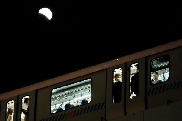 أشخاص يركبون قطارًا خلال خسوف للقمر فوق سماء طوكيو، اليابان 8 نوفمبر 2022. - سبوتنيك عربي