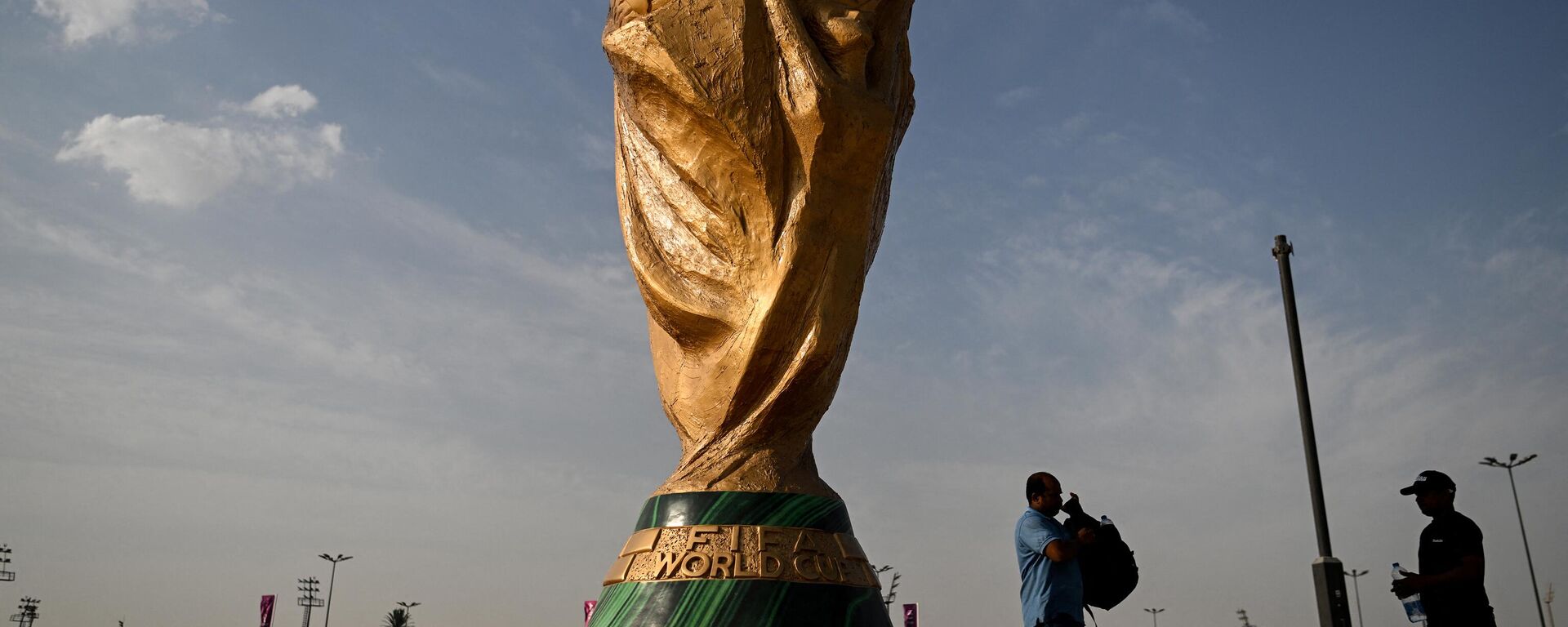 رجال يمشون أمام نسخة طبق الأصل من كأس العالم لكرة القدم خارج استاد أحمد بن علي في الريان في 12 نوفمبر 2022 ، قبل بطولة كأس العالم لكرة القدم قطر 2022. - سبوتنيك عربي, 1920, 20.11.2022