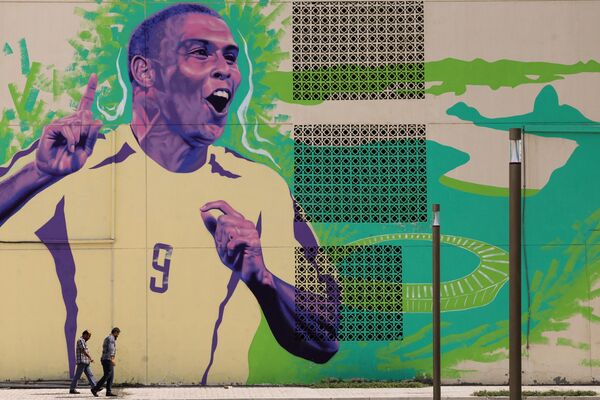 رجال يسيرون أمام لوحة جدارية للمهاجم البرازيلي السابق رونالدو في الدوحة في 6 نوفمبر 2022، قبل بدء بطولة كأس العالم لكرة القدم قطر 2022. - سبوتنيك عربي