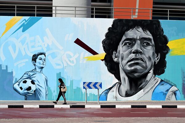 امرأة تمر من أمام لوحة جدارية تصور أسطورة كرة القدم الأرجنتينية دييغو مارادونا بالقرب من ملعب خليفة الدولي في الدوحة في 18 نوفمبر 2022، قبل انطلاق بطولة كأس العالم لكرة القدم قطر 2022. - سبوتنيك عربي