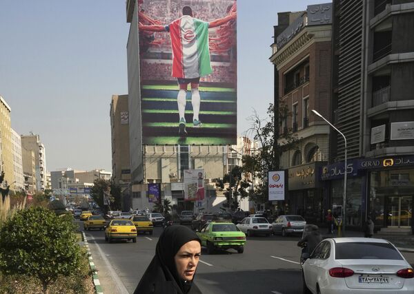 لوحة جدارية ترعاها الدولة تظهر لاعب كرة قدم وطني مع علم الدولة يدخل إلى ملعب معلقة على مبنى في وسط مدينة طهران، إيران، 22 نوفمبر 2022 - سبوتنيك عربي