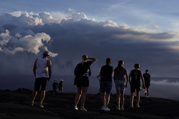 الناس يقفون على صخرة الحمم البركانية من ثوران سابق بالقرب من بركان ماونا لوا أثناء اندلاعه، بالقرب من هيلو، هاواي 30 نوفمبر 2022 - سبوتنيك عربي