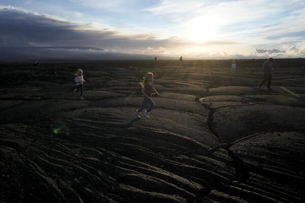 أطفال يركضون على صخور الحمم البركانية السوداء من ثوران سابق بالقرب من بركان ماونا لوا أثناء ثورانه، بالقرب من هيلو، هاواي.  30 نوفمبر 2022 - سبوتنيك عربي