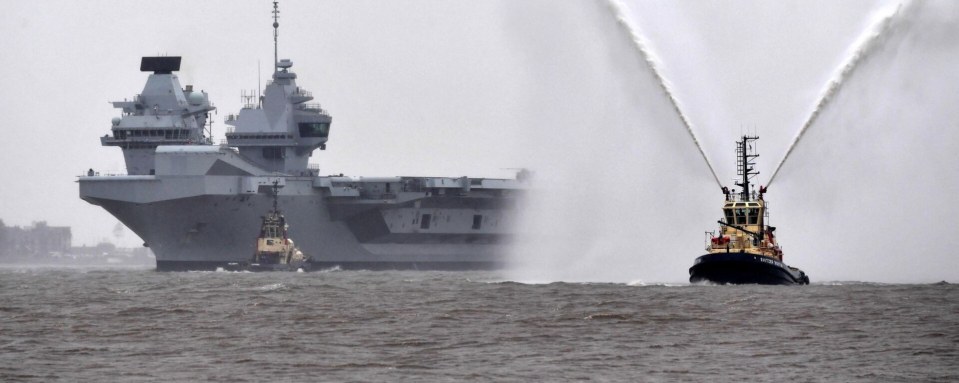 قارب سحب يرش الماء في الهواء أثناء ترحيبه بحاملة الطائرات إتش إم إس برينس أوف ويلز التابعة للبحرية الملكية البريطانية في عام 2020  - سبوتنيك عربي, 1920, 26.12.2022