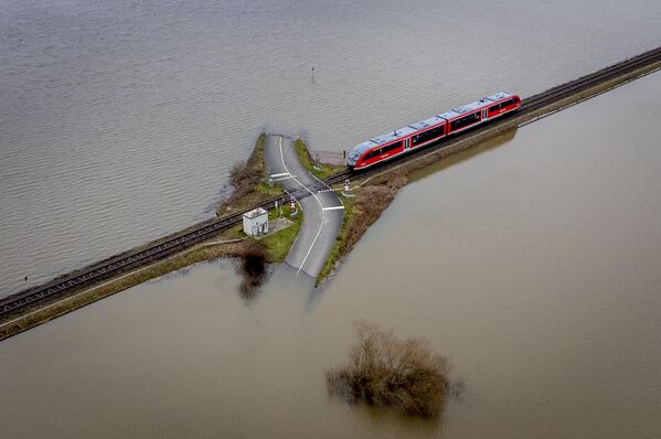 قطار إقليمي يقترب من معبر للسكك الحديدية بين الحقول التي غمرتها الفيضانات في نيديراو-إتشين بالقرب من فرانكفورت، ألمانيا، 16 يناير 2023. - سبوتنيك عربي