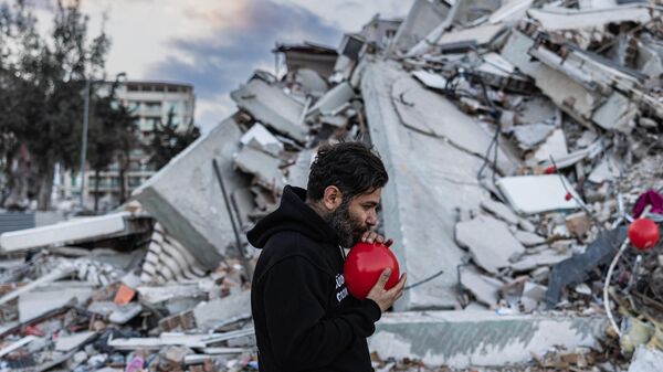أوغون سيفير أوكيور، رجل تركي، يبلغ من العمر 38 عامًا، يربط بالونًا لتعليقه على حطام مبنى منهار في أنطاكيا، جنوب تركيا في 21 فبراير 2023 - سبوتنيك عربي