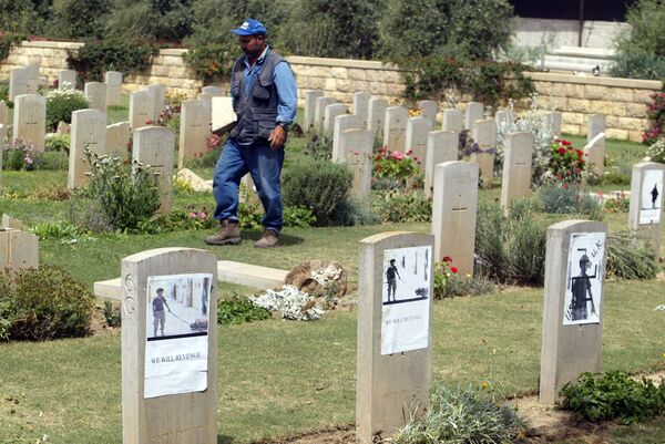 حارس مقبرة يحمل حجر قبر مكسور بينما يسير على خلفية صور لسجناء عراقيين يتعرضون للإساءة والإذلال من قبل القوات الأمريكية في سجن أبو غريب في العراق، ملصقة على حجارة قبور أخرى عليها نقوش انتقامية، بعد تعرض مقبرة لجنود بريطانيين قُتلوا خلال الحرب العالمية الأولى في شمال مدينة غزة للتخريب، 10 مايو 2004. يومها قال عصام جرادة، المسؤول عن صيانة المقبرة، إنه &quot;هو ووالده منع المخربين، وبعضهم كانوا مسلحين، من تدنيس أكثر من 4000 مقبرة معظمها بريطانية&quot;. - سبوتنيك عربي