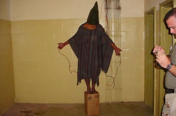 هذه صورة حصلت عليها وكالة &quot;أسوشيتيد برس&quot; الأمريكية، تظهر  فيها محتجزًا مجهول الهوية يقف على صندوق مع حقيبة على رأسه وأسلاك كهربائية مثبتة على يديه في سجن أبو غريب في بغداد، أواخر عام 2003. - سبوتنيك عربي