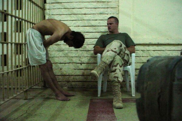 هذه صورة حصلت عليها &quot;وكالة أسوشيتيد برس&quot; تظهر فيها معتقلًا عراقيًا منحنيًا ويداه ممسكة بقضبان زنزانة سجن بينما يراقبه جندي في سجن أبو غريب في بغداد، أواخر عام 2003. - سبوتنيك عربي